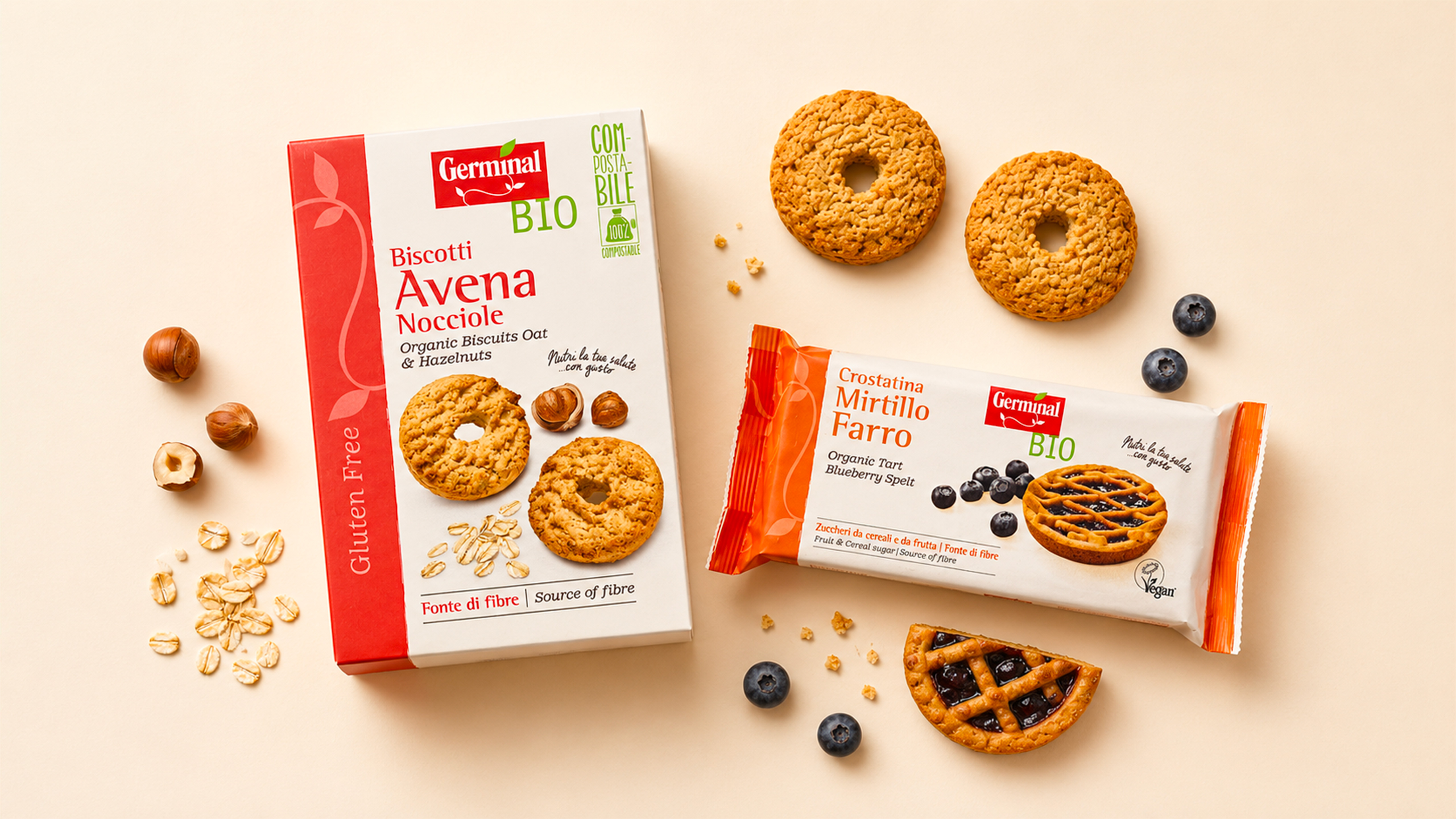 Confezioni germinal bio di biscotti allavena e nocciole e crostatina al mirtillo e farro con biscotti nocciole fiocchi davena e mirtilli su sfondo beige