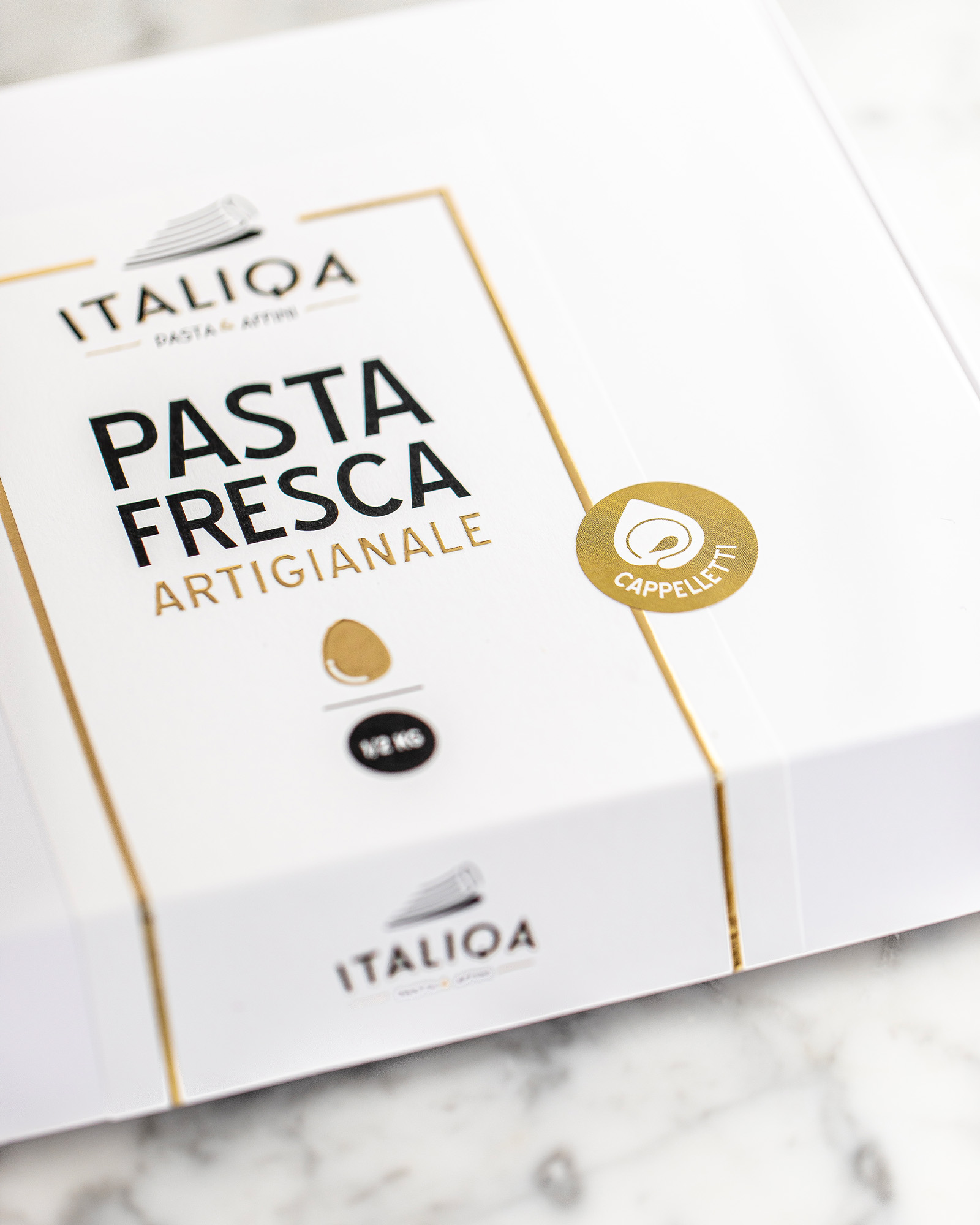 Dettaglio della confezione bianca e oro di pasta fresca artigianale italiqa cappelletti su superficie in marmo