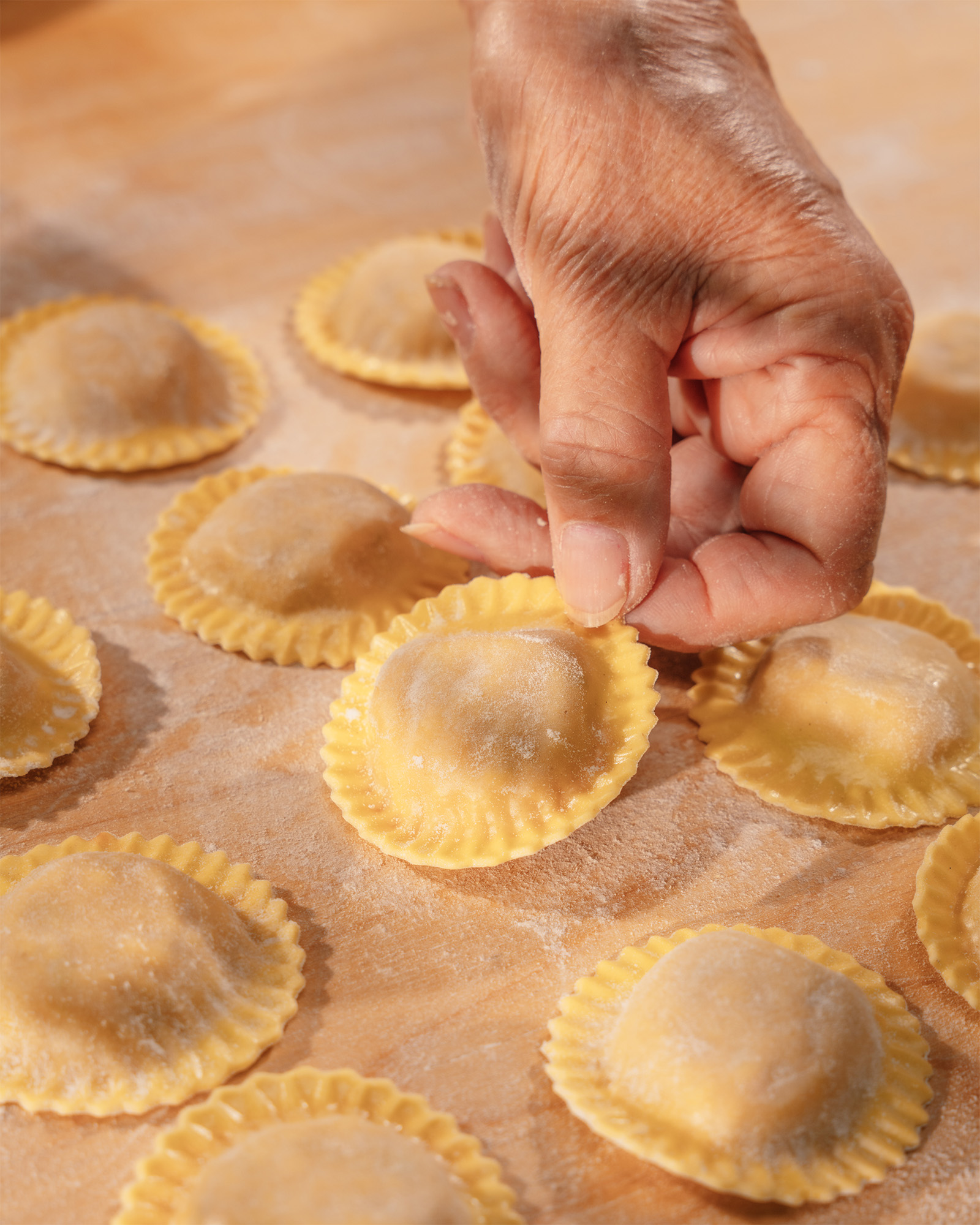 Mano che solleva un raviolo fresco tra diversi ravioli disposti su un piano infarinato