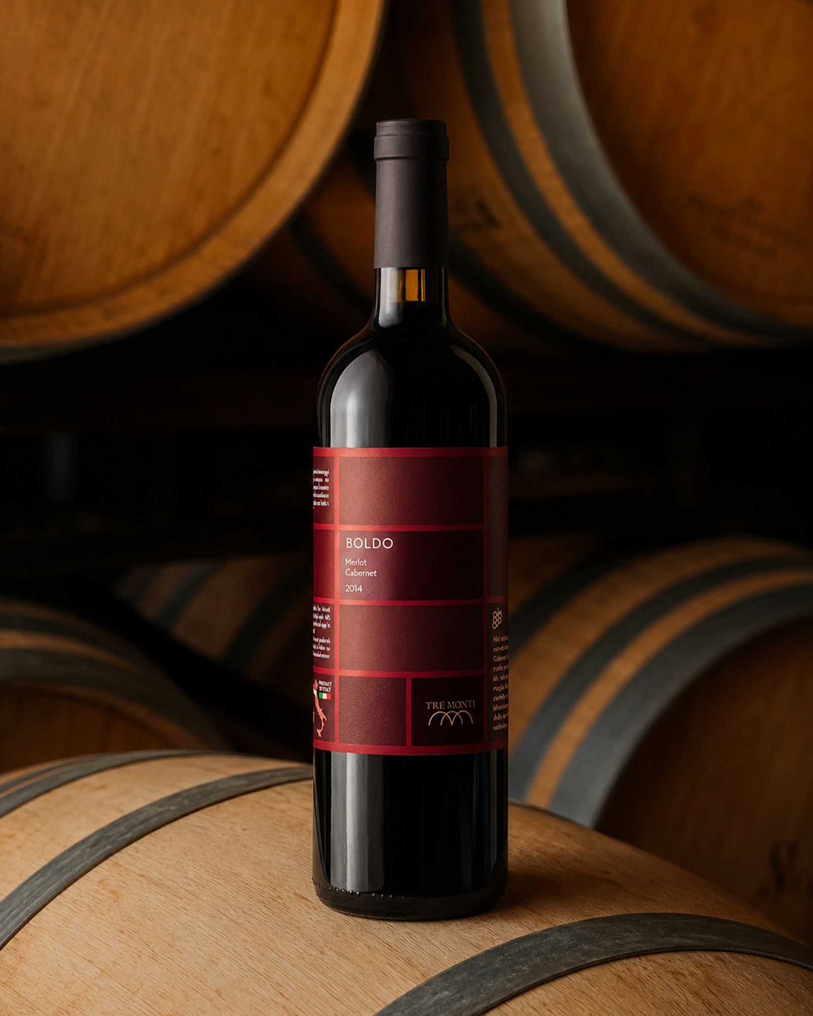 Bottiglia di vino boldo merlot cabernet 2014 tre monti posata su una botte di legno in cantina