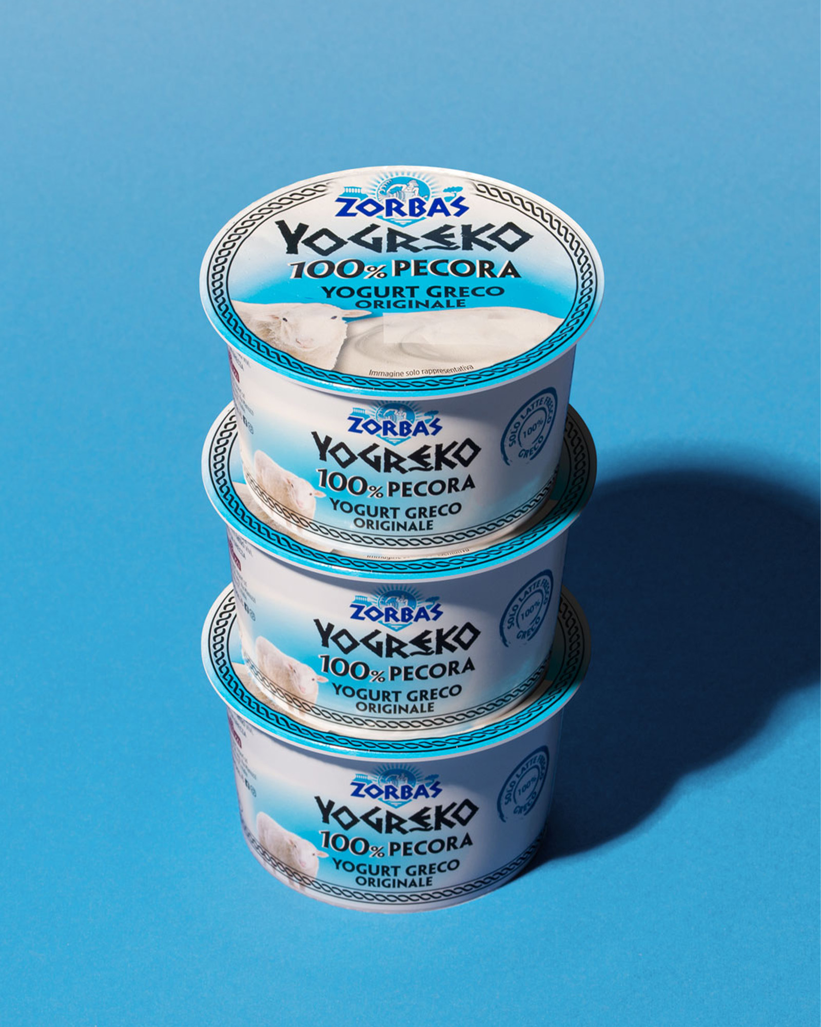 Tre confezioni sovrapposte di yogurt greco zorbas cento per cento pecora su sfondo azzurro